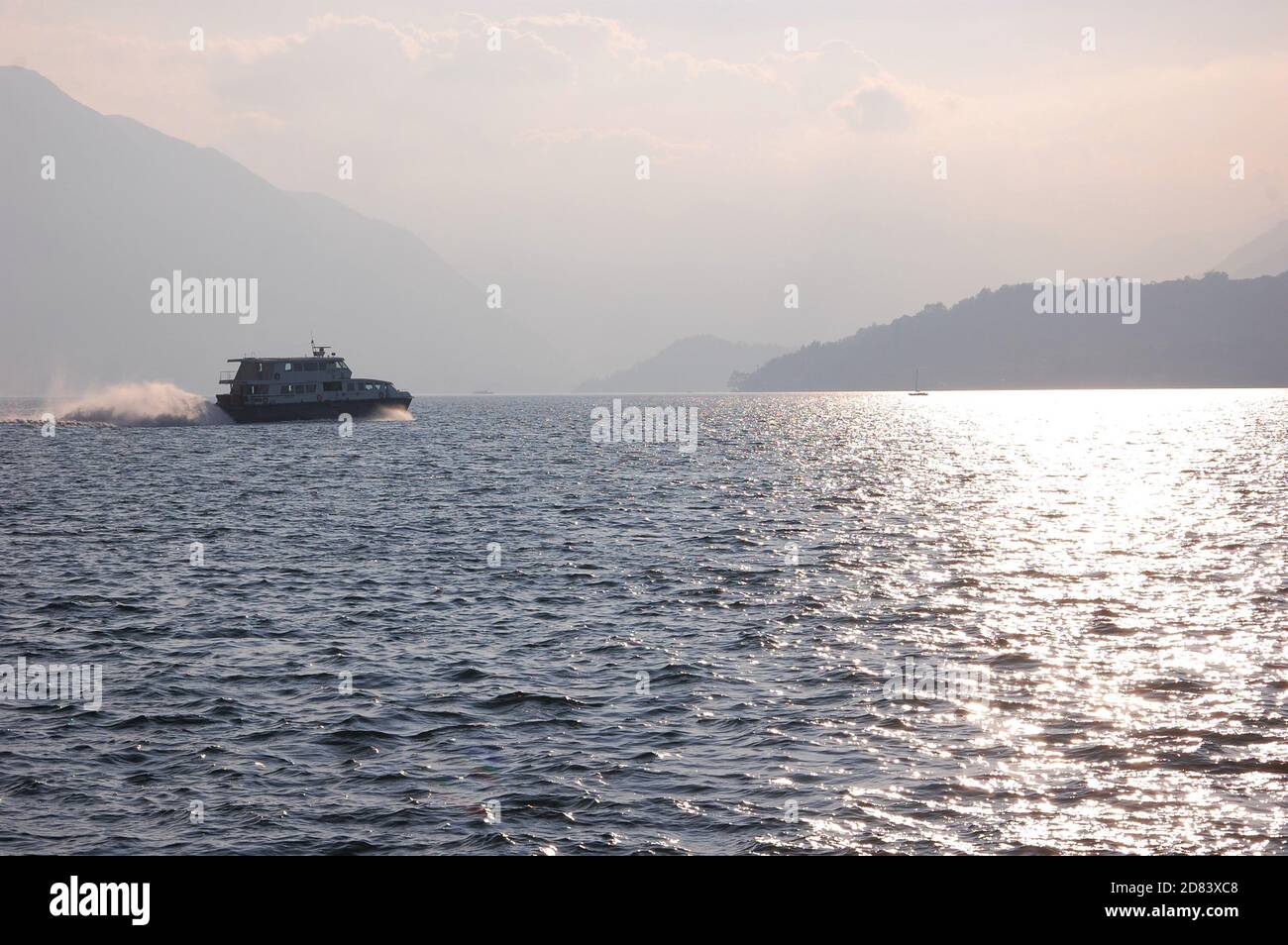 Les passagers de l'embarcation traversant rapidement le lac de Côme de départ Varenna avec des silhouettes de montagnes en contre-jour dans un après-midi d'automne Banque D'Images