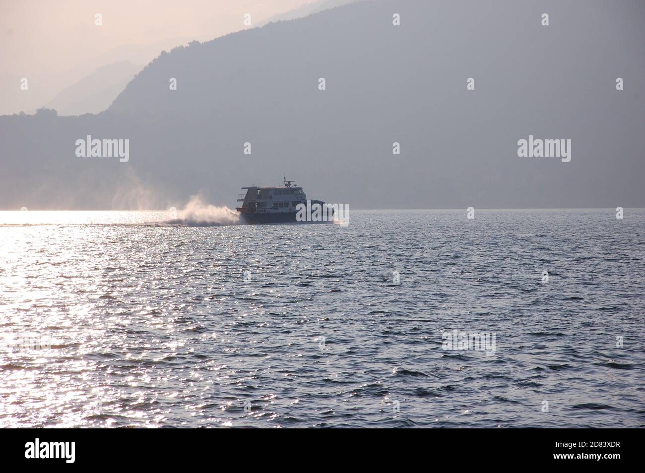 Les passagers de l'embarcation traversant rapidement le lac de Côme de départ Varenna avec des silhouettes de montagnes en contre-jour dans un après-midi d'automne Banque D'Images