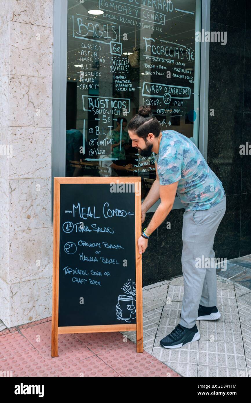 Jeune serveur plaçant un tableau noir avec le menu quotidien à l'extérieur Banque D'Images