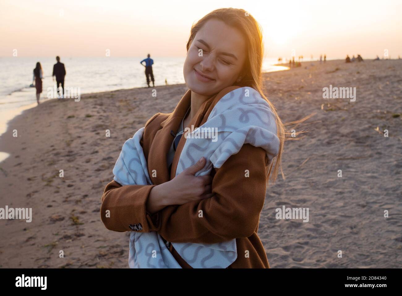 Jeune belle femme enveloppée dans une couverture chaude, chaude et confortable sur la plage. Courir sur la plage au coucher du soleil, se sentir libre et heureux. Banque D'Images