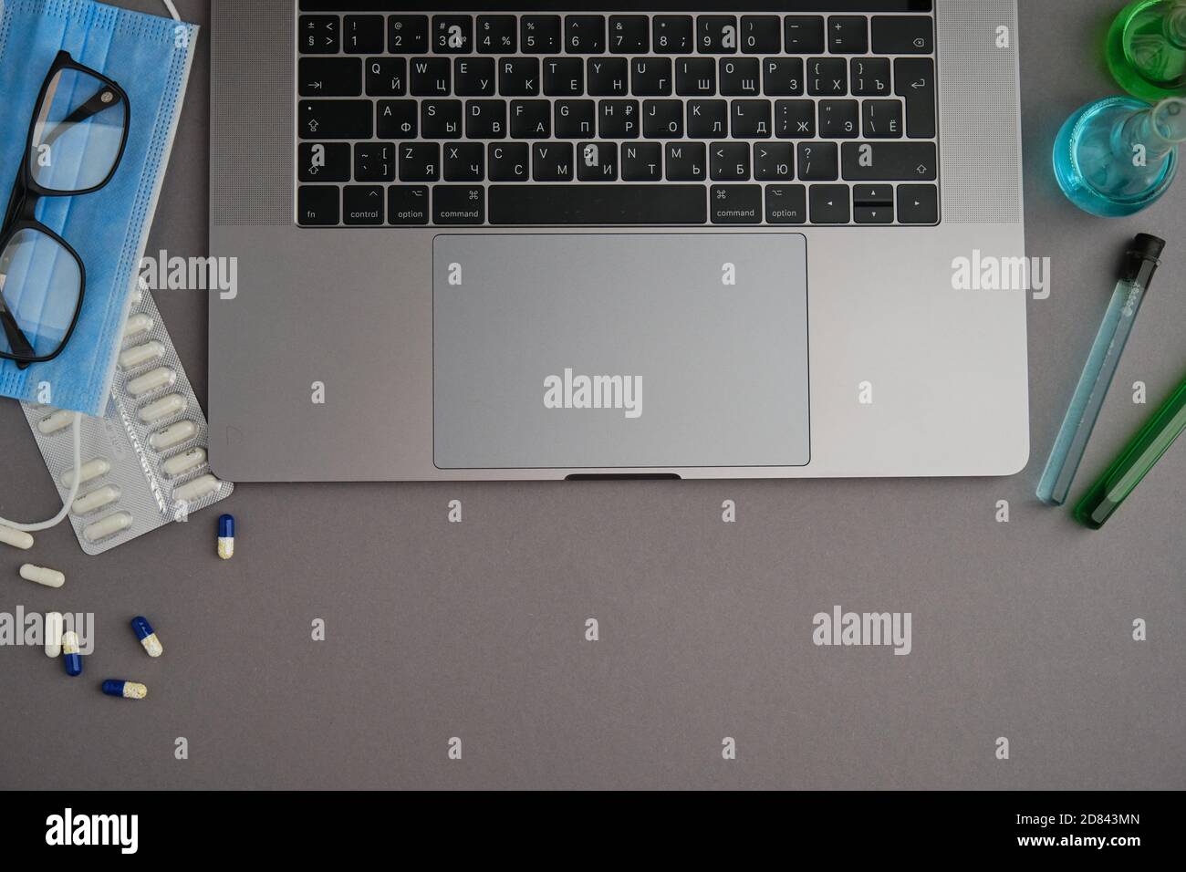 Plat d'ordinateur portable, tubes médicaux et flacon, masque et lunettes sur un bureau gris. Travailler à domicile. Virus et auto-isolement Banque D'Images