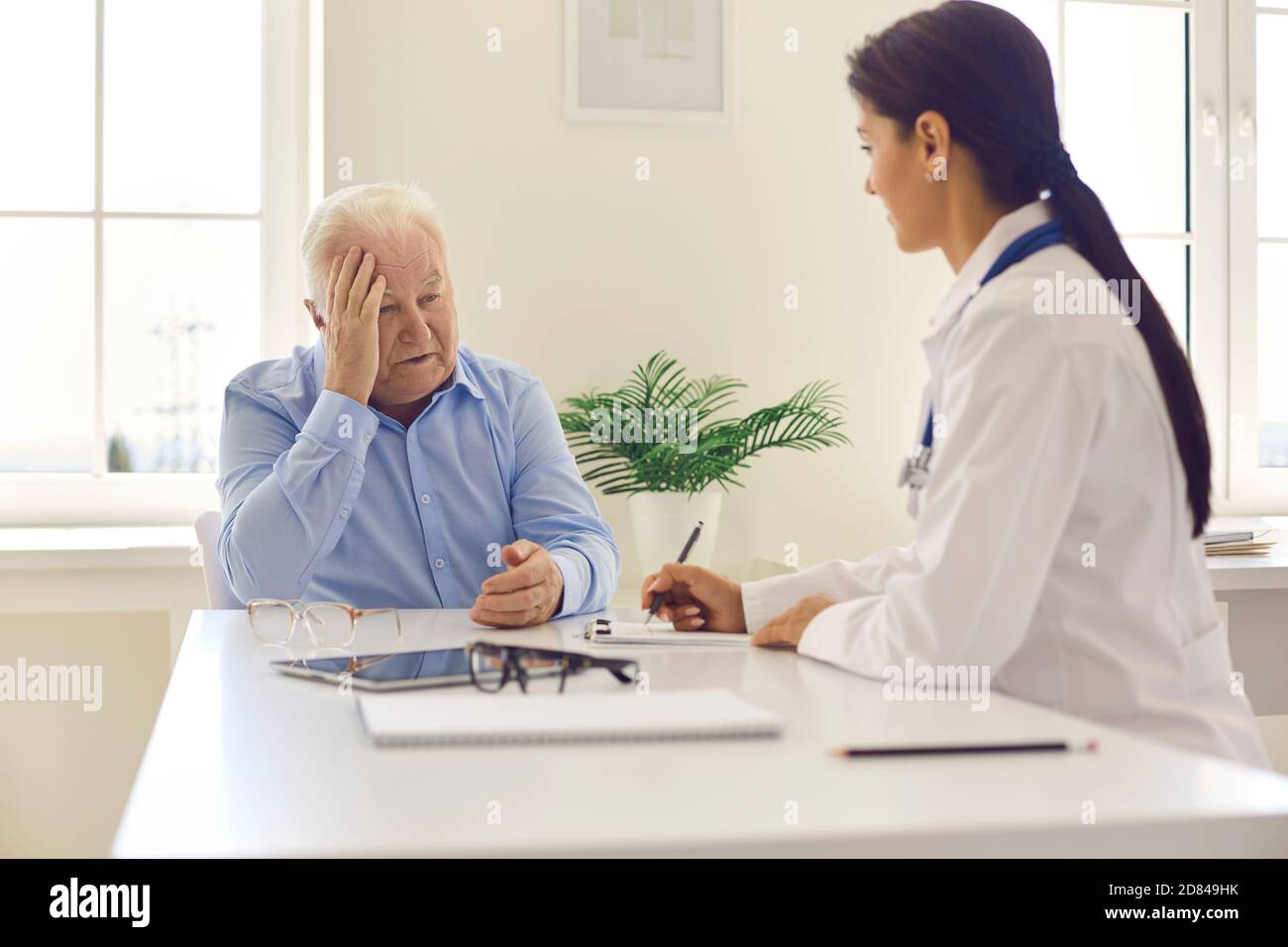 Un patient âgé se plaint de maux de tête chez une jeune femme positive médecin Banque D'Images