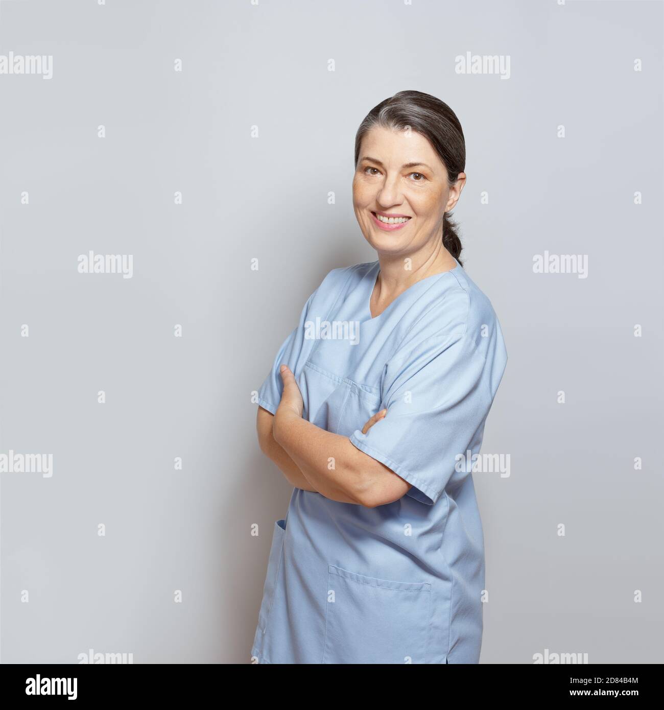Infirmière mûre souriante et amicale dans un gommage bleu, un arrière-plan clair, un espace de texte ou de copie. Banque D'Images