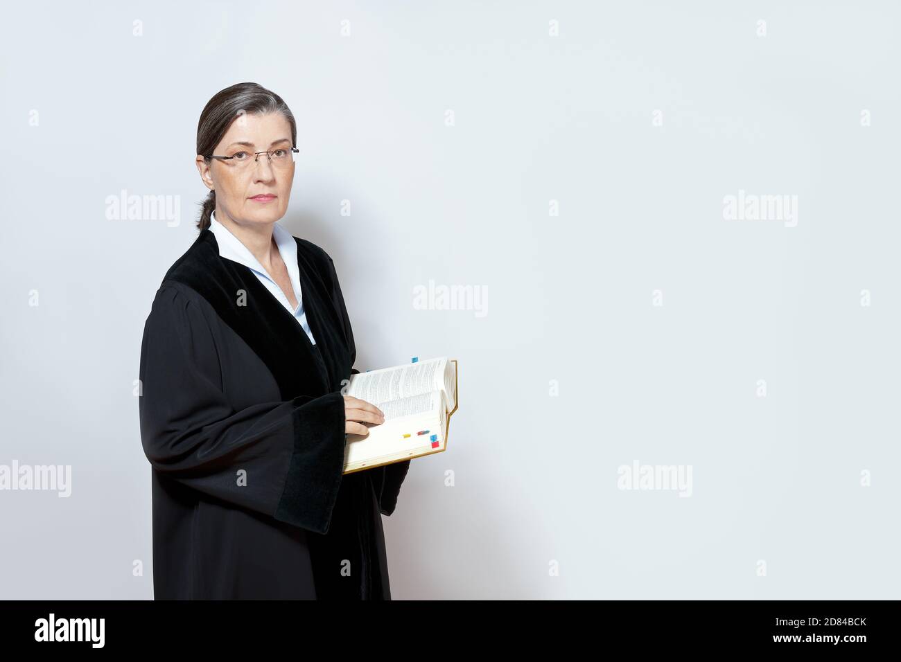 Femme d'âge moyen juge en robe noire avec un livre de droit, un fond neutre, un espace de copie. Banque D'Images