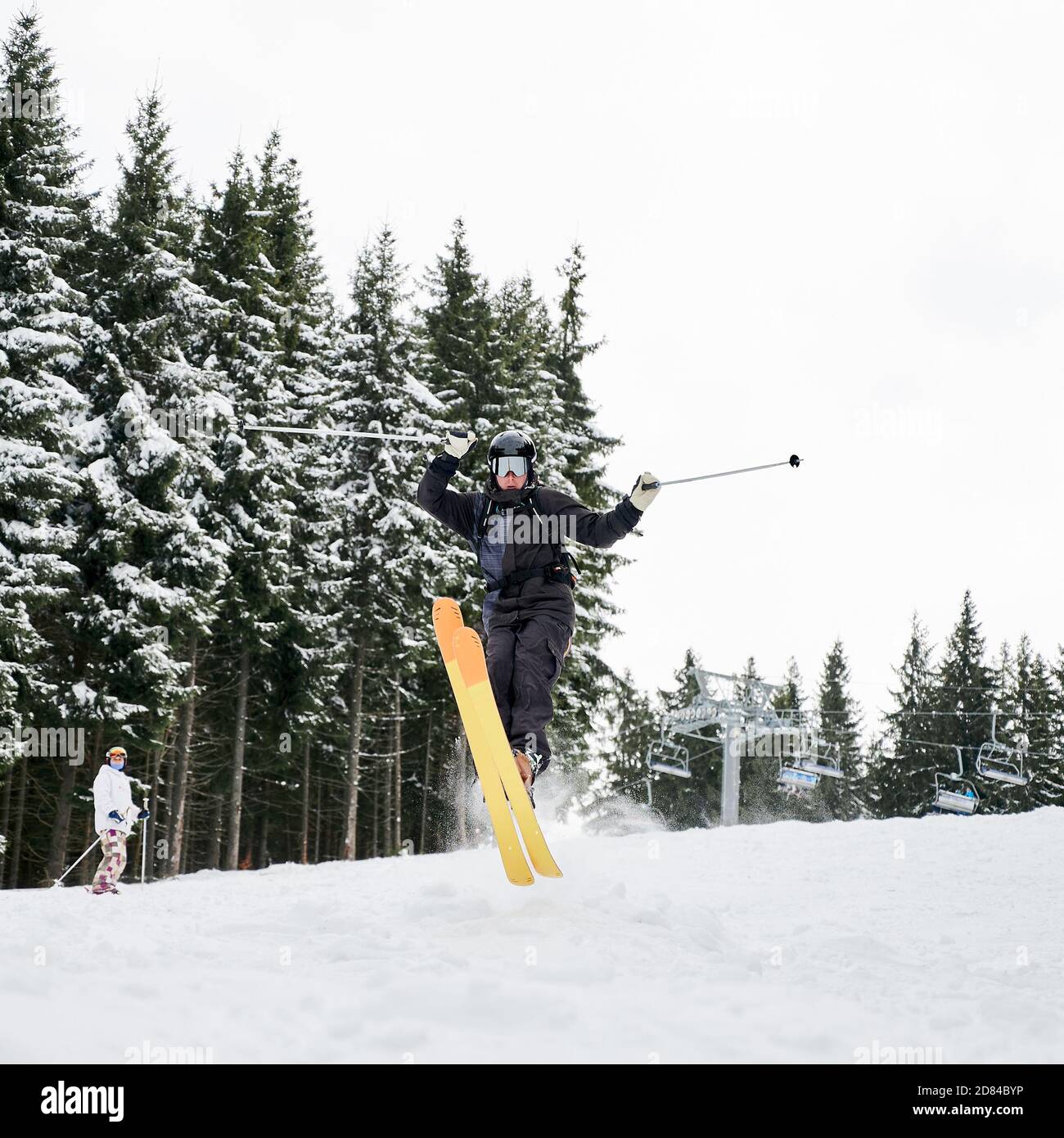 Skieur mâle skier sur de la neige poudreuse fraîche avec des pins enneigés en arrière-plan. Homme freerider tenant des bâtons de ski et faisant sauter tout en glissant sur les pistes enneigées. Concept de sport d'hiver extrême Banque D'Images