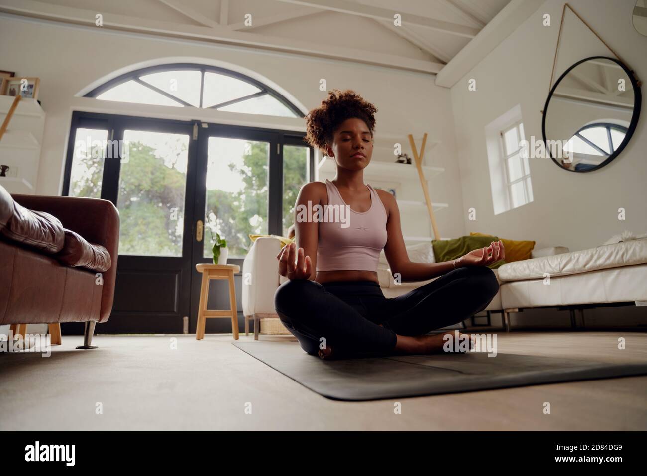 Vue en contre-plongée d'une jeune femme en forme physique tapis à la maison en position lotus tout en méditant Banque D'Images