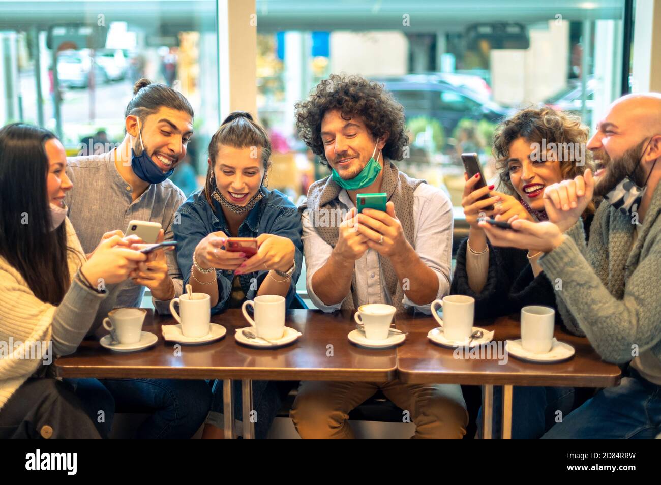 Deux hommes regardant dans le téléphone au-dessus de l'épaule de fille ami et essayant de voir ce qui est sur l'écran, dans le café boutique - Groupe d'ami heureux avec le Banque D'Images