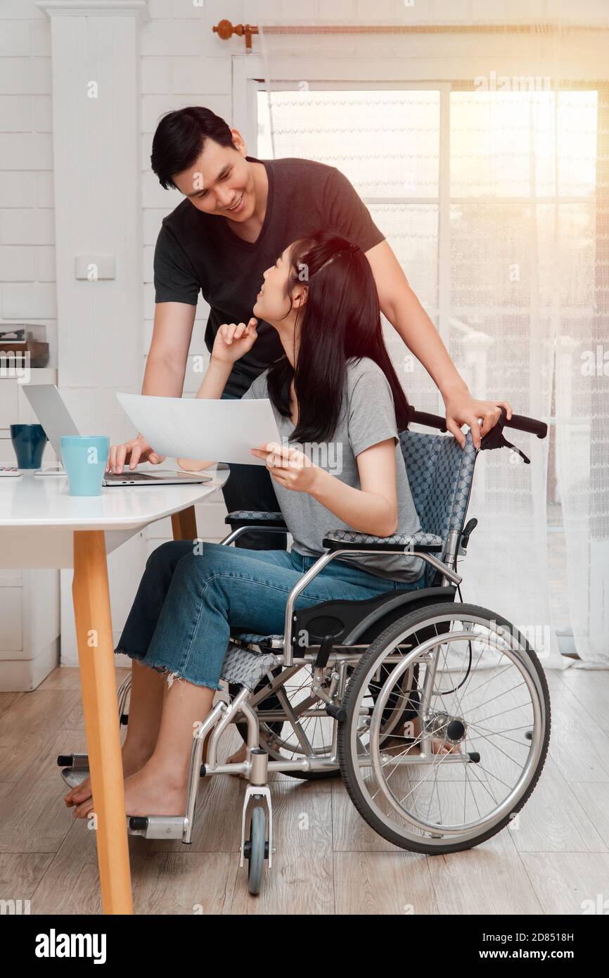 Une femme en fauteuil roulant après un accident de voiture et travaillant avec un ordinateur à la maison avec son amant. Le concept de soins mutuels et de nouvelles technologies est fou Banque D'Images