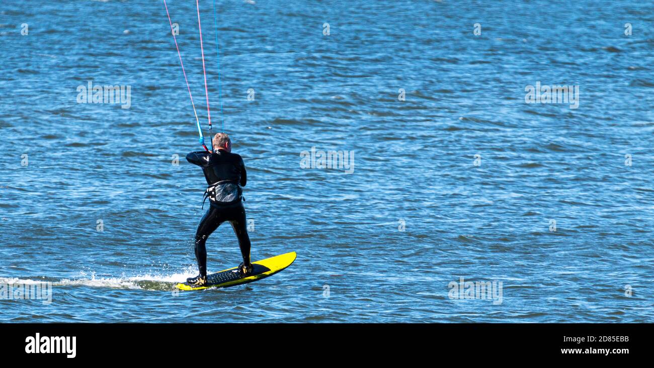 Un homme est kite surf sur un plateau de surf jaune dans la longue île son portant une suite humide. Banque D'Images