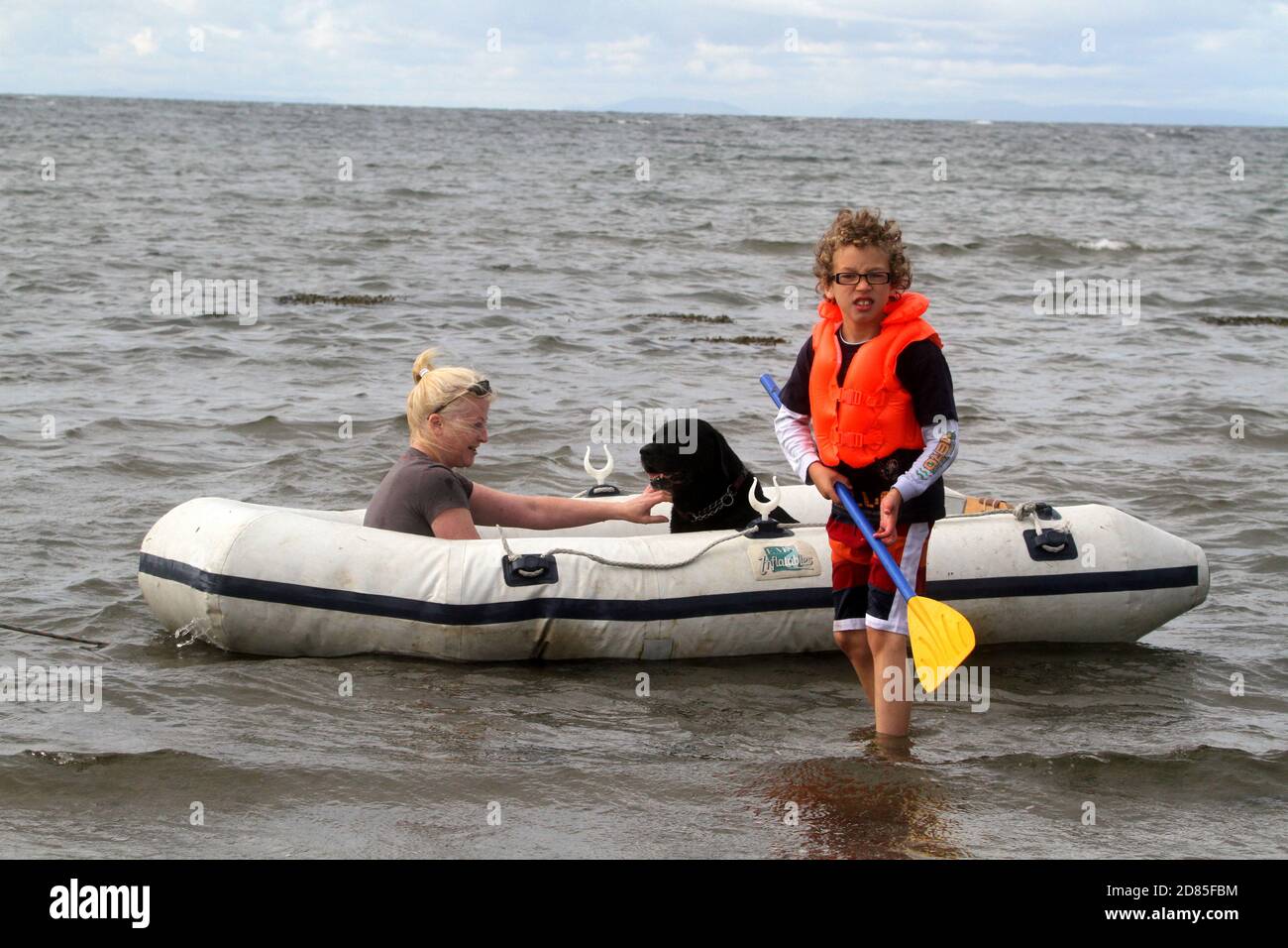 Maidens, Ayrshire, Écosse, Royaume-Uni. Un jeu en famille dans la mer avec un canot en caoutchouc parents adulte tenant avec l'enfant portant un gilet de sauvetage Banque D'Images