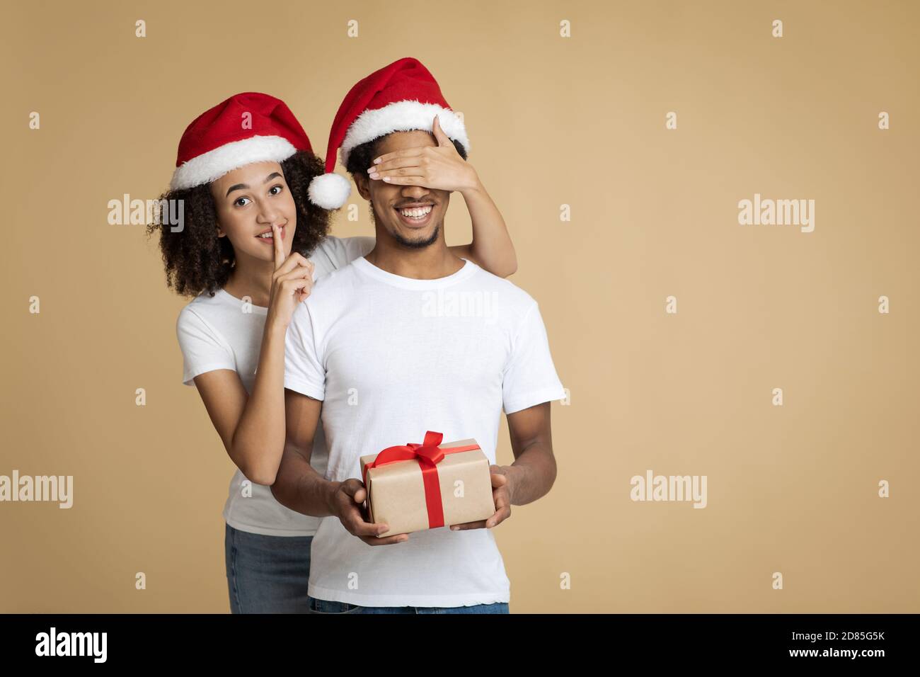 Joyeuse femme africaine américaine à Santa Hat montre le signe de silence avec la main et ferme les yeux au mari Banque D'Images