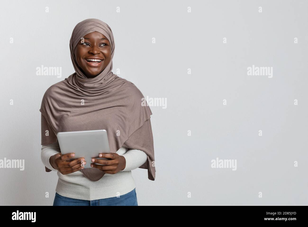 Joyeuse femme musulmane noire en hijabposant avec la tablette numérique plus arrière-plan clair Banque D'Images