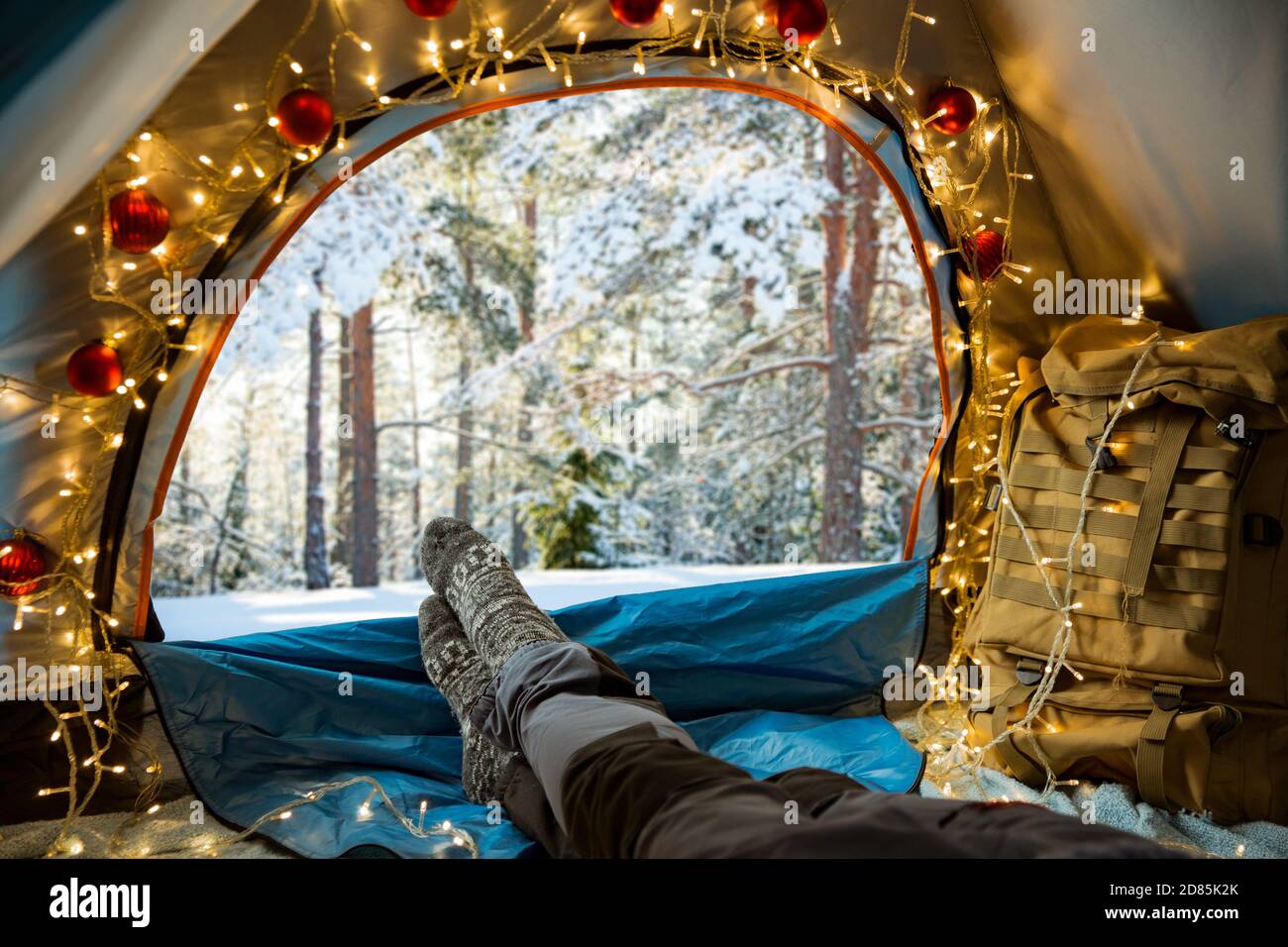 Un homme allongé dans une tente décorée de lumières de Noël portant du bois chaud. Belle forêt sauvage d'hiver couverte de neige. Auto-isolation Banque D'Images