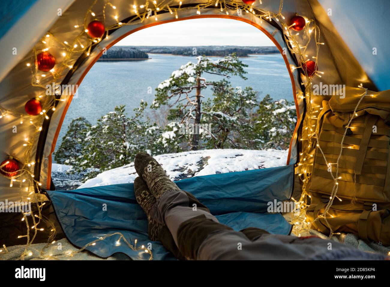 Un homme allongé dans une tente décorée de lumières de Noël portant du bois chaud. Belle forêt sauvage d'hiver couverte de neige. Auto-isolation Banque D'Images