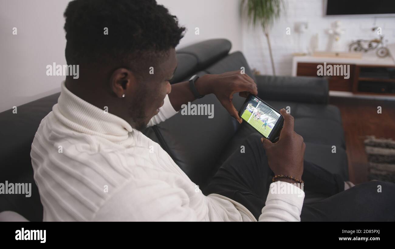 Jeune homme noir excité regardant un match de football sur le smartphone. Photo de haute qualité Banque D'Images