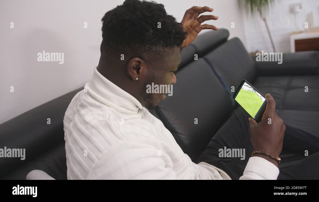 Jeune homme noir excité regardant un match de football sur le smartphone. Photo de haute qualité Banque D'Images