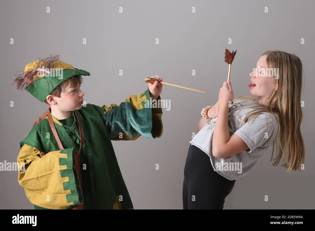 Un jeune garçon espiègle vêtu de Robin des Bois, faisant semblant de tirer des flèches sur la sœur sœur sœur sœur aînée pendant le jeu de rôle. Banque D'Images