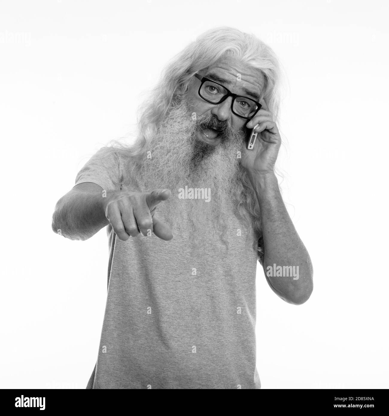 Studio shot of happy senior homme barbu smiling while talking on mobile phone and pointing at camera Banque D'Images