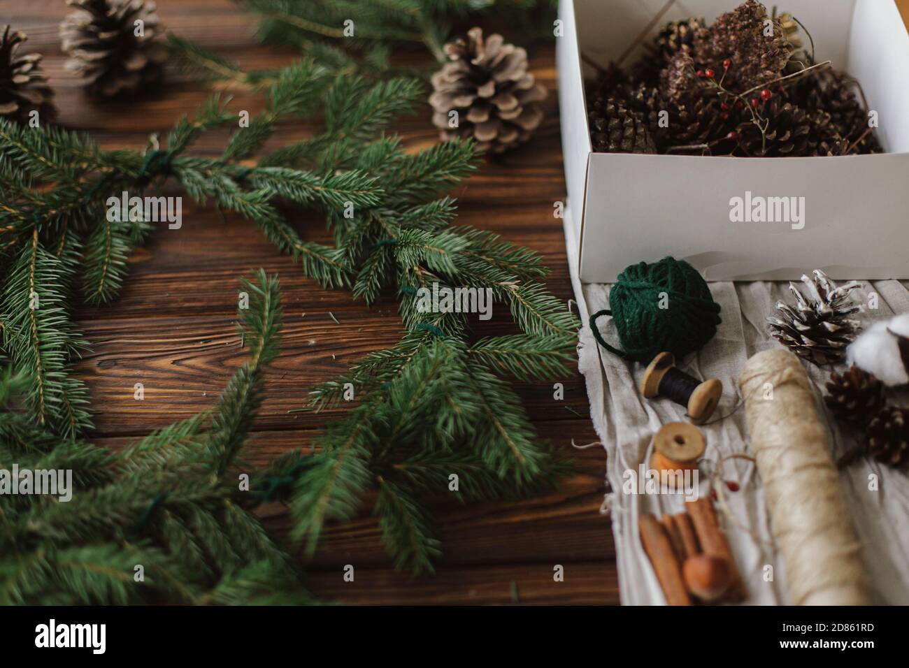 Fabrication d'une couronne de noël rustique sur une table en bois. Couronne de Noël avec baies, branches vertes, cônes de pin et décorations de fête naturelles, ciseaux, t Banque D'Images