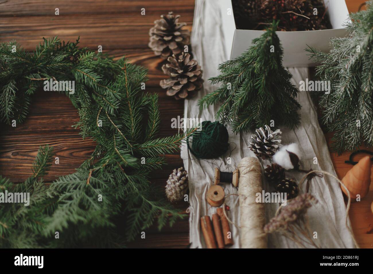 Fabrication d'une couronne de noël rustique sur une table en bois. Couronne de Noël avec baies, branches vertes, cônes de pin et décorations de fête naturelles, ciseaux, t Banque D'Images