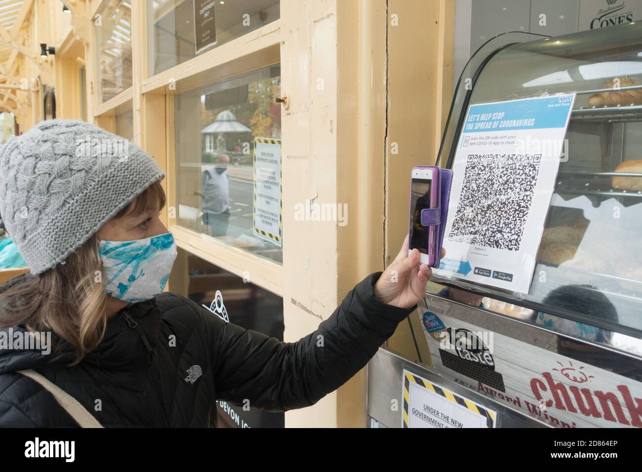 Une dame avec masque de visage utilise son smartphone pour scanner le code QR NHS pour entrer un lieu pour le système de suivi. Banque D'Images