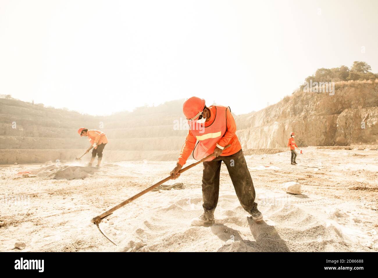 Les mineurs travaillant avec l'outil d'extraction dans la poussière et la cuisson chaude, l'exploitation minière et l'été chaud soleil dans les arrière-plans. Un concept de travail acharné. Bruit, grain. Banque D'Images