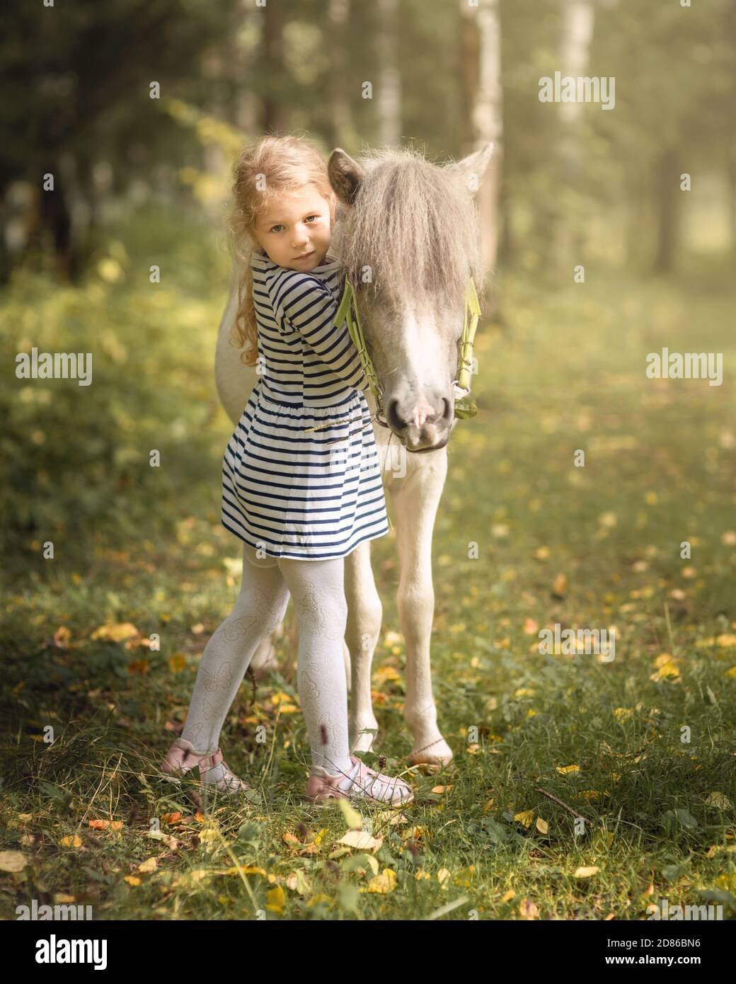 La petite fille blonde est debout près du poney du petit cheval et de l'embrasser Banque D'Images
