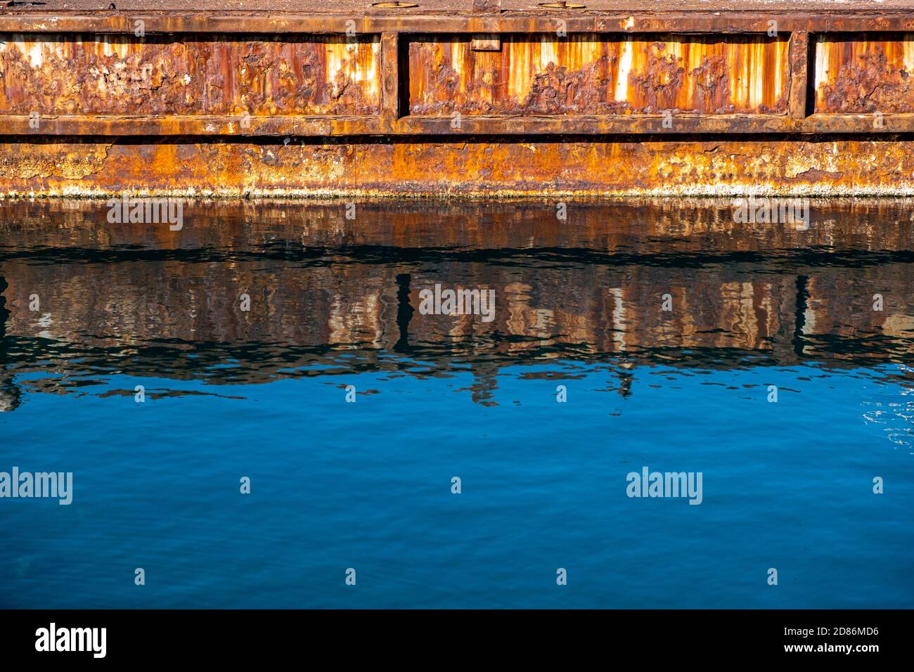 Vieux port industriel en métal rouillé réflexions sur l'eau de mer bleu clair. Banque D'Images