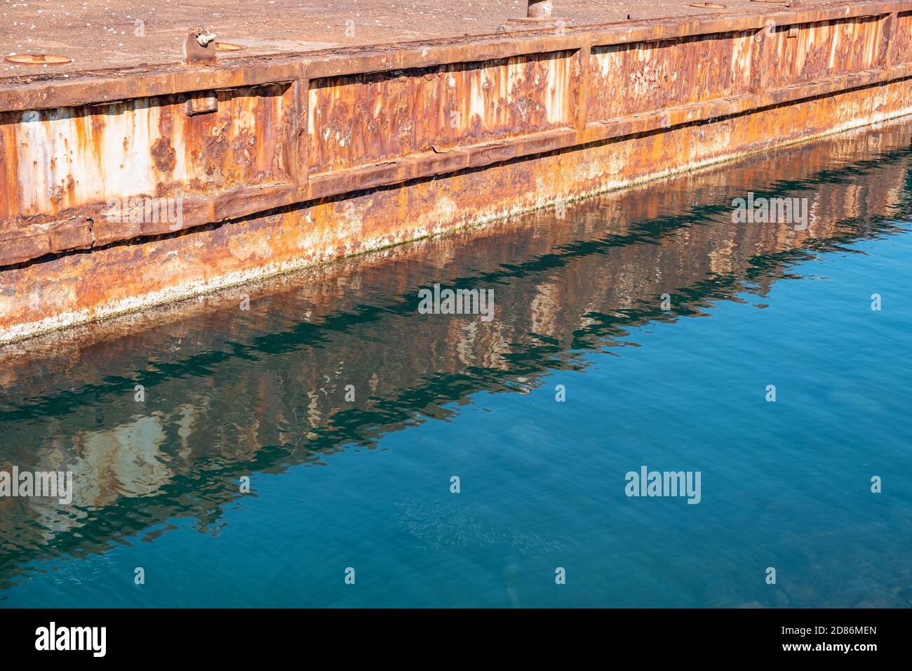 Vieux port industriel en métal rouillé réflexions sur l'eau de mer bleu clair. Banque D'Images