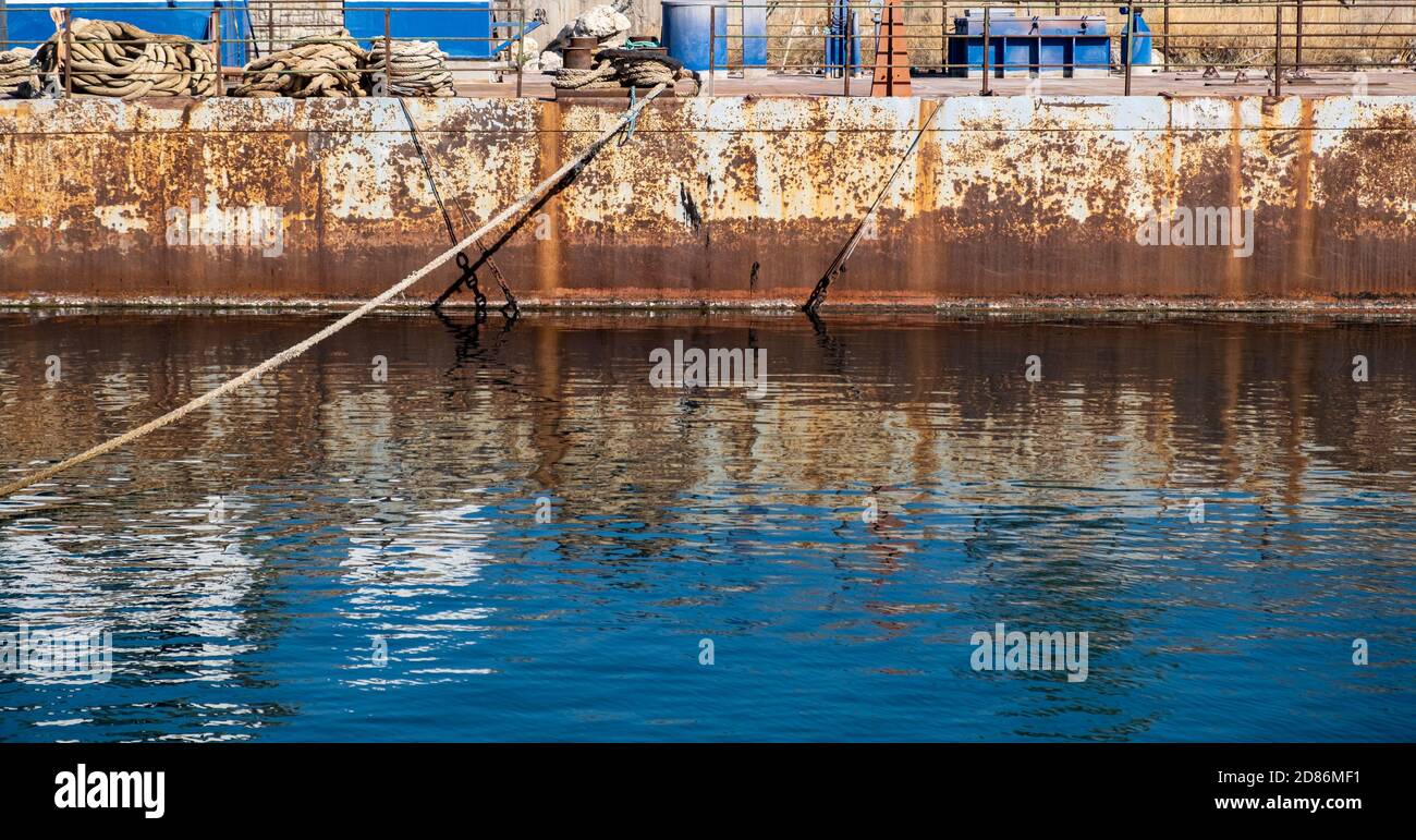 Cordes d'amarrage attachées sur bollardσ acier sur un pont rouillé de port. Les navires se sécurisent amarrés sur un vieux quai industriel, réflexions sur l'eau de mer Banque D'Images