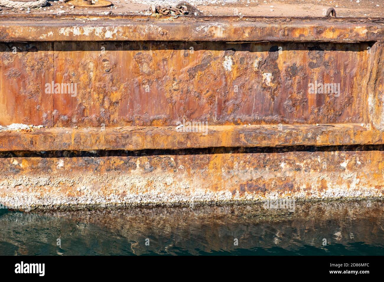 Vieux quai industriel en métal rouillé près du port, réflexions sur l'eau de mer. Banque D'Images
