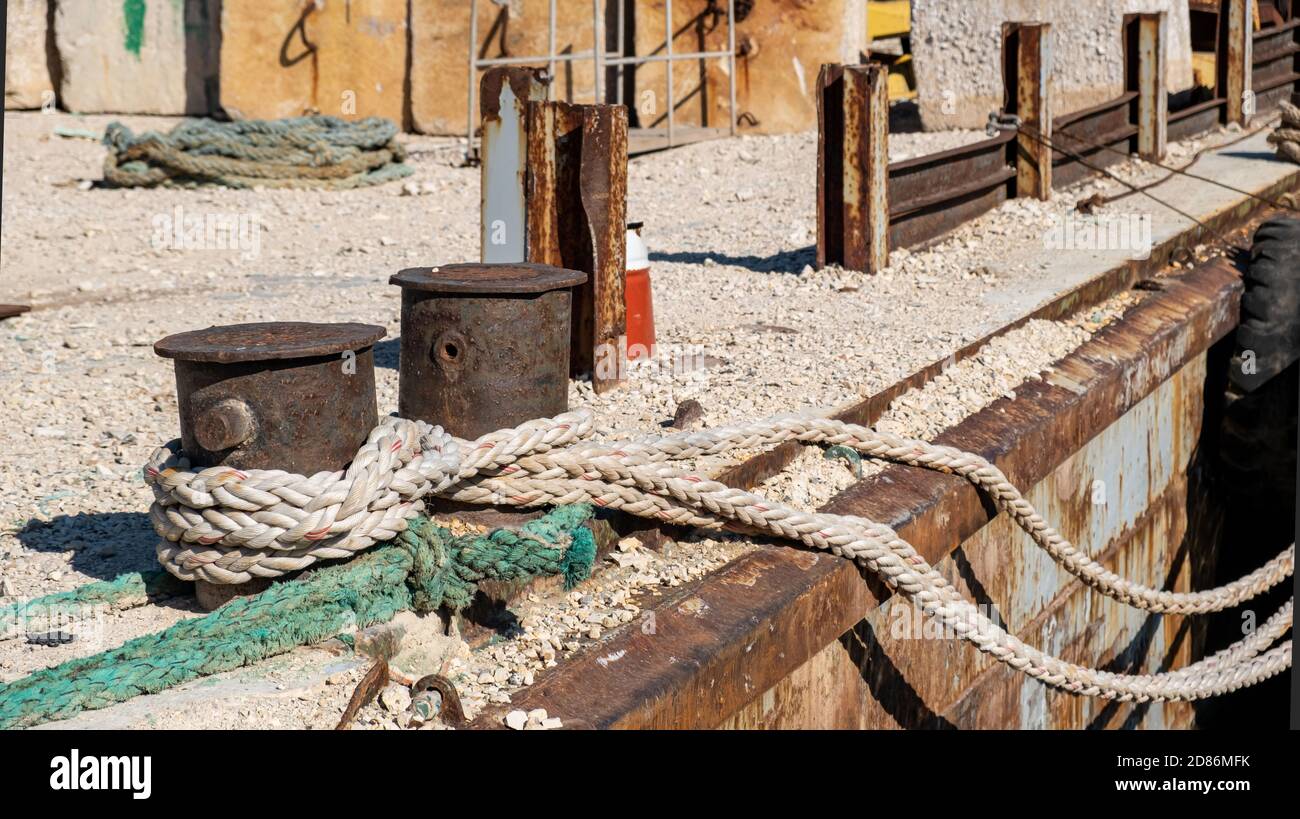 Cordes d'amarrage attachées sur un bollard en acier rouillé sur un pont. Les navires sont amarrés sur un vieux quai de port industriel Banque D'Images