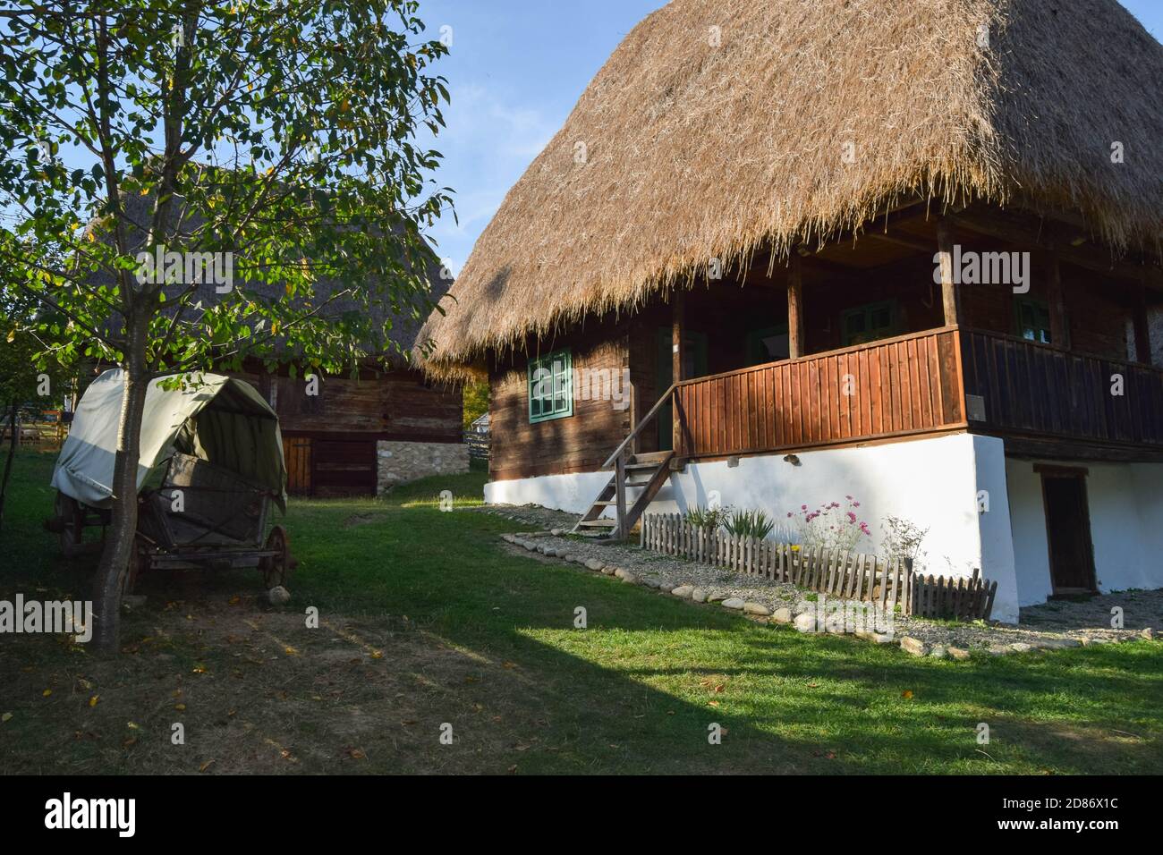 Maison rurale traditionnelle roumaine avec murs en bois, petites fenêtres, toit de chaume. Architecture nationale. Soleil chaud jour de printemps. Banque D'Images