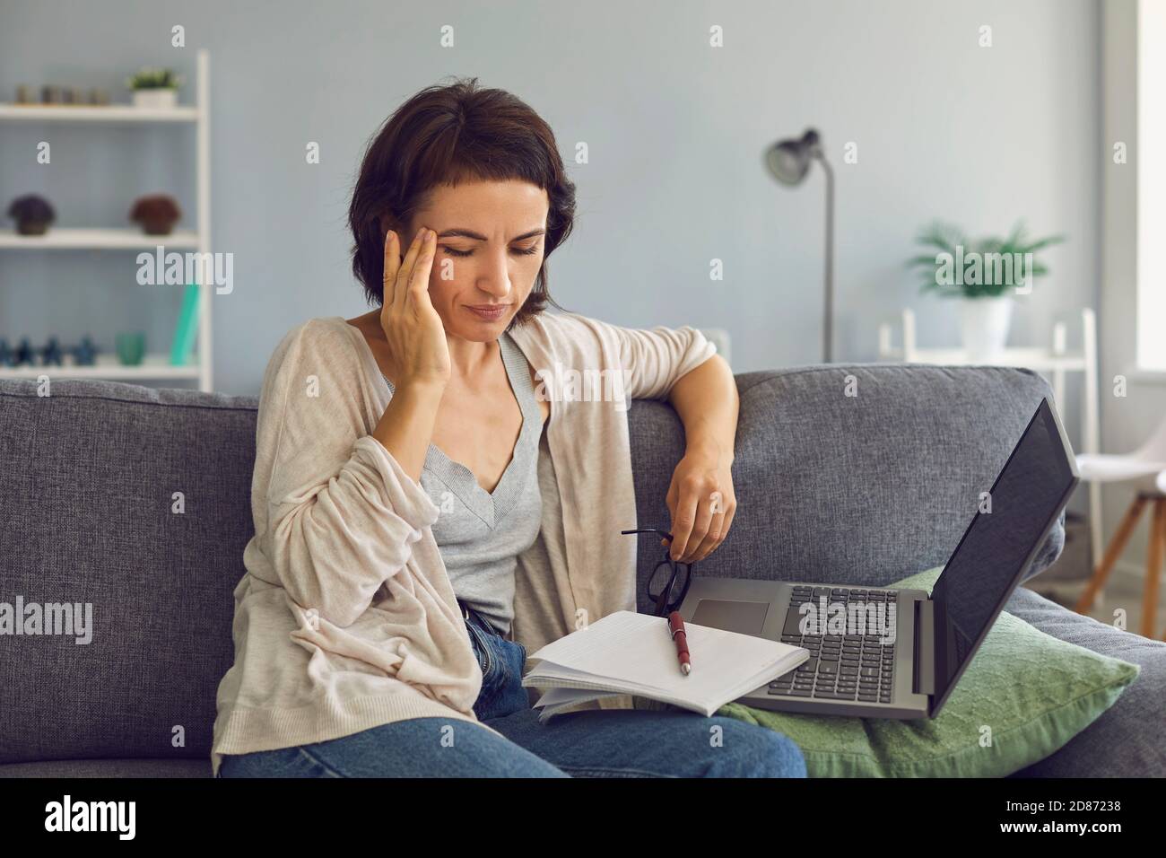Femme fatiguée et stressée assise à la maison près d'un ordinateur portable et d'un ordinateur portable et sensation de mal de tête Banque D'Images