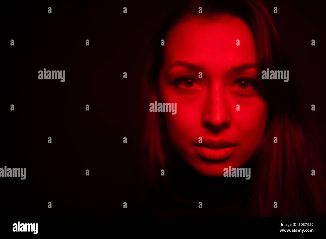 portrait d'une jolie fille regardant l'appareil photo a dilaté l'élève dans espace de copie lumière rouge Banque D'Images