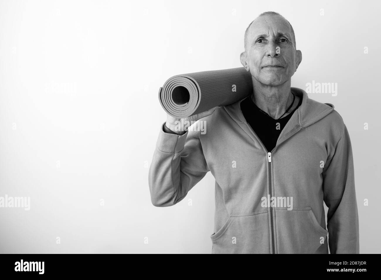 Studio shot of bald senior man holding yoga mat prêt pour sport against white background Banque D'Images