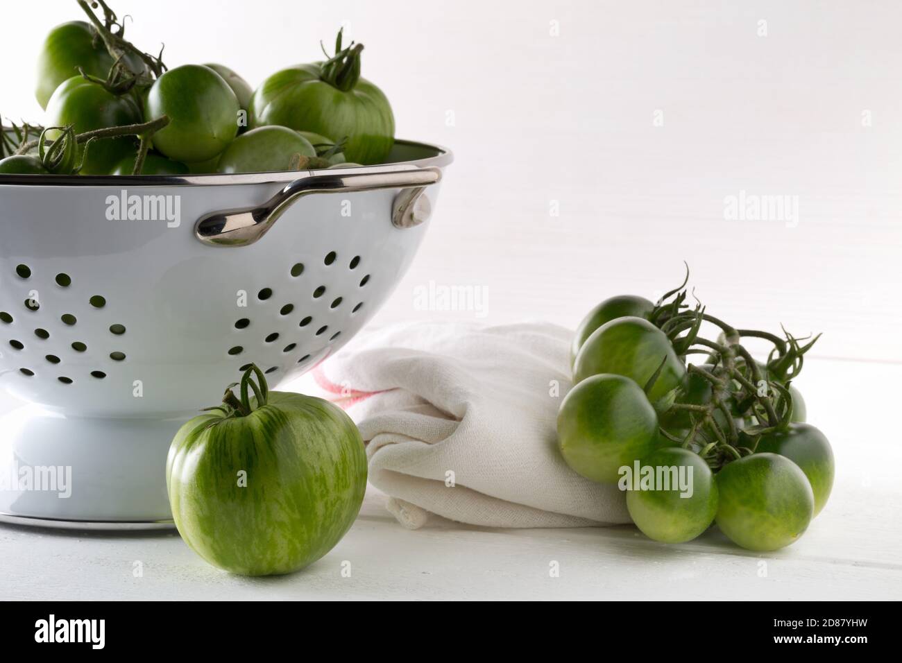 Tomates vertes non mûres en passoire et sur table en bois blanc fond de cuisine, les tomates non mûres peuvent être frites ou utilisées pour la mise au point relish et sélective Banque D'Images