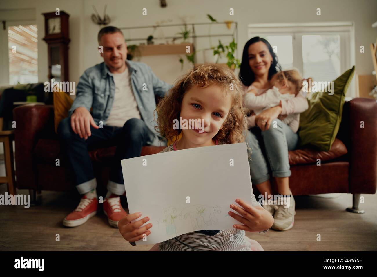 Portrait d'une fille souriante montrant des œuvres d'art sur papier etage avec détente en famille sur le canapé Banque D'Images