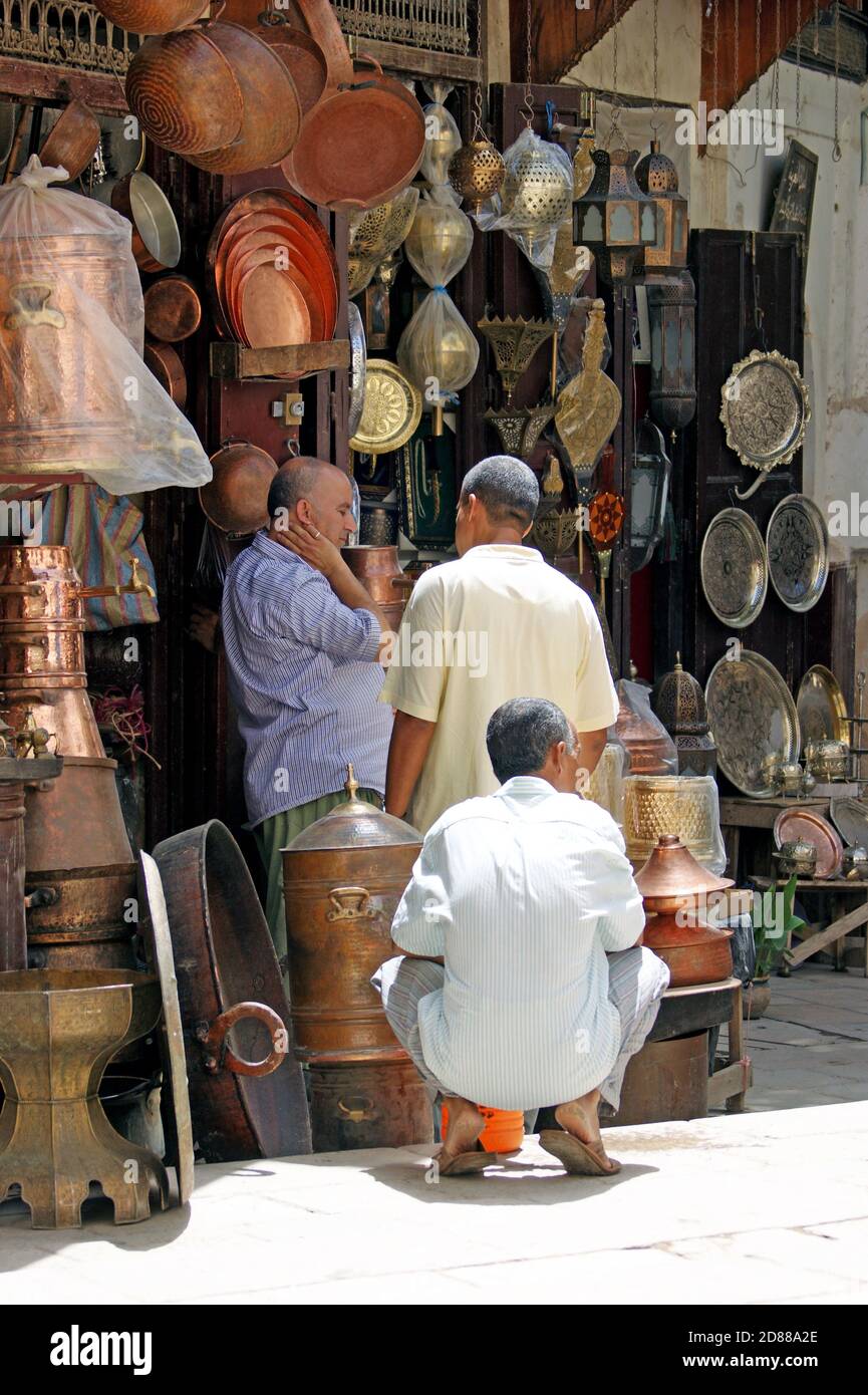 Trois hommes marocains parlent à l'extérieur d'une boutique de souvenirs métalliques dans la vieille médina de Fès, au Maroc. Banque D'Images
