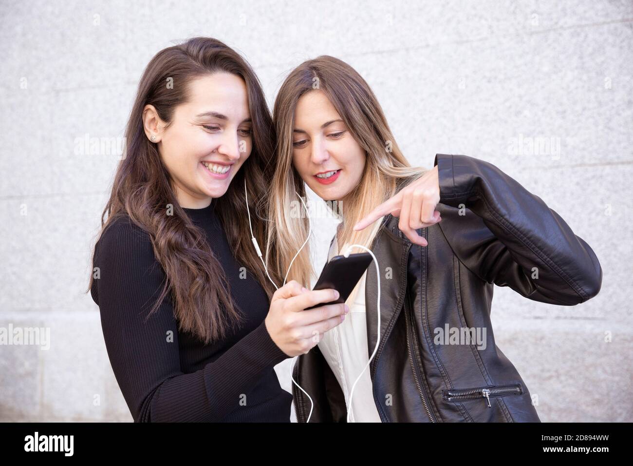 Deux amis heureux partageant un téléphone portable pour écouter de la musique dans la rue. Banque D'Images