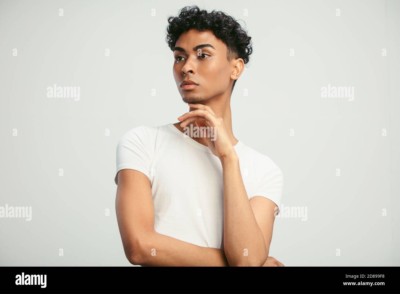 Portrait d'un jeune homme debout avec sa main sur le menton et regardant loin. Homme androgyne sur fond blanc. Banque D'Images