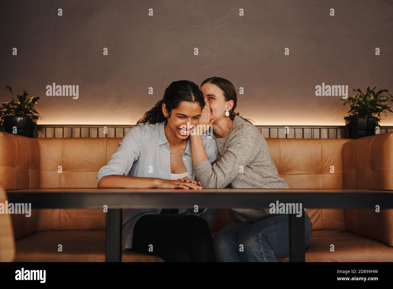 Femme chuchotant un secret dans l'oreille d'un autre ami. Deux amies assises dans un café-restaurant et potins. Banque D'Images
