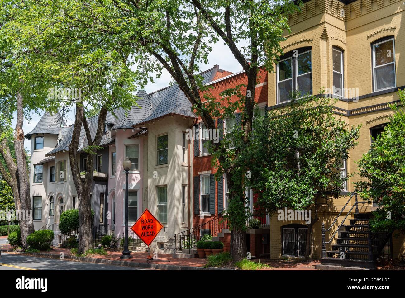 Un mélange de tourelles carrées et rondes élaborées ornent une rangée de maisons colorées dans une rue Q Street, NW, Georgetown, Washington, DC bordée d'arbres. Banque D'Images