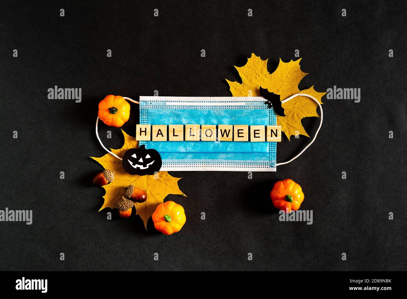 Citrouilles d'Halloween, masque médical protecteur et feuilles d'érable jaune sur fond noir, chauves-souris en papier noir. L'inscription HALLOWEEN le Banque D'Images