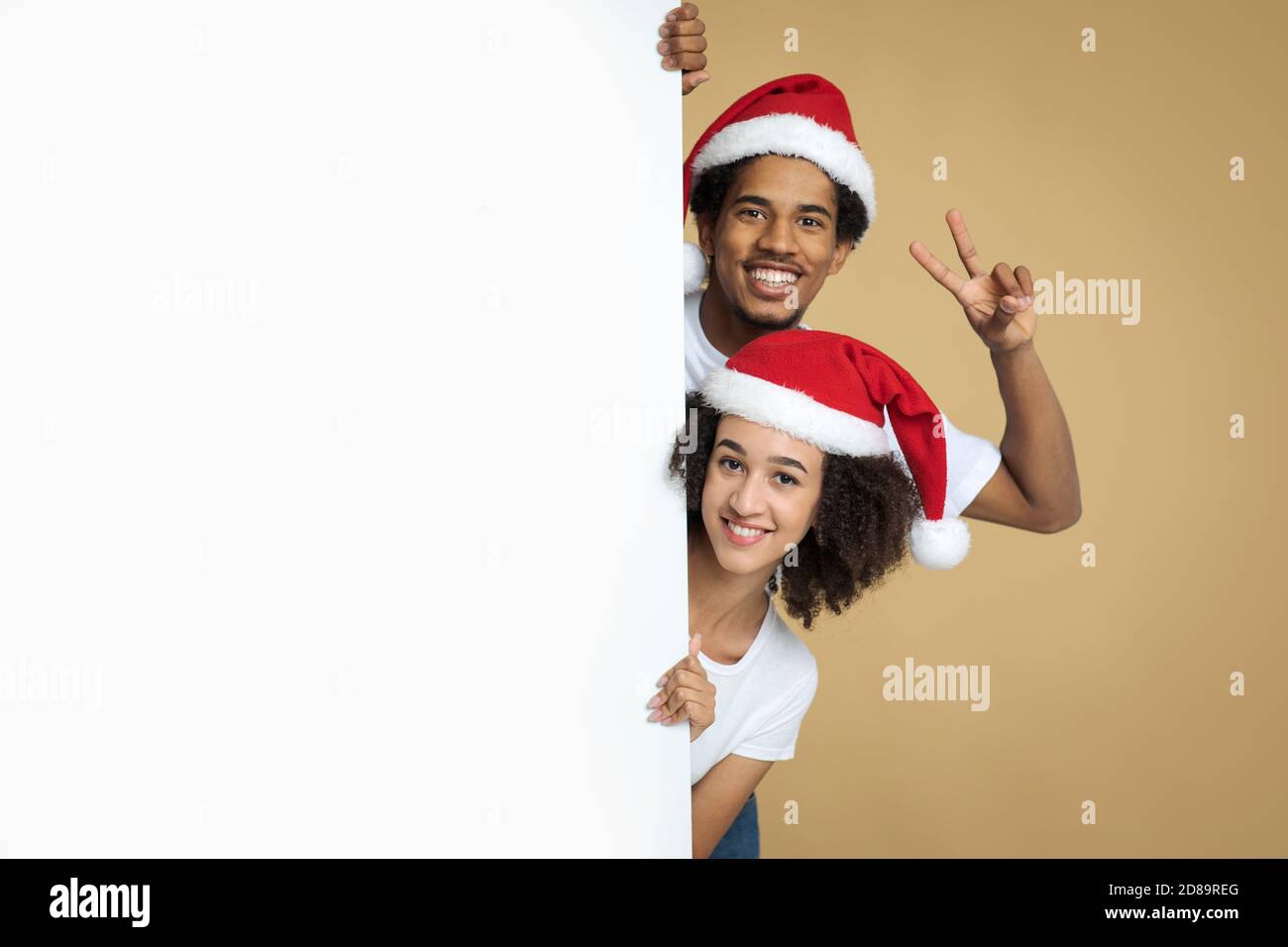 Un jeune couple afro-américain souriant dans des chapeaux de Noël qui se déllent derrière une bannière blanche Banque D'Images