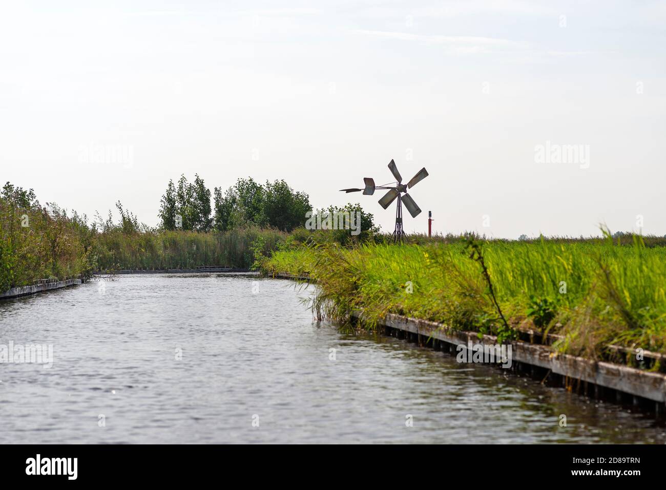 Un moulin à vent en métal se tenant sur la rive d'un canal qui coule dans une rivière aux pays-Bas. Banque D'Images