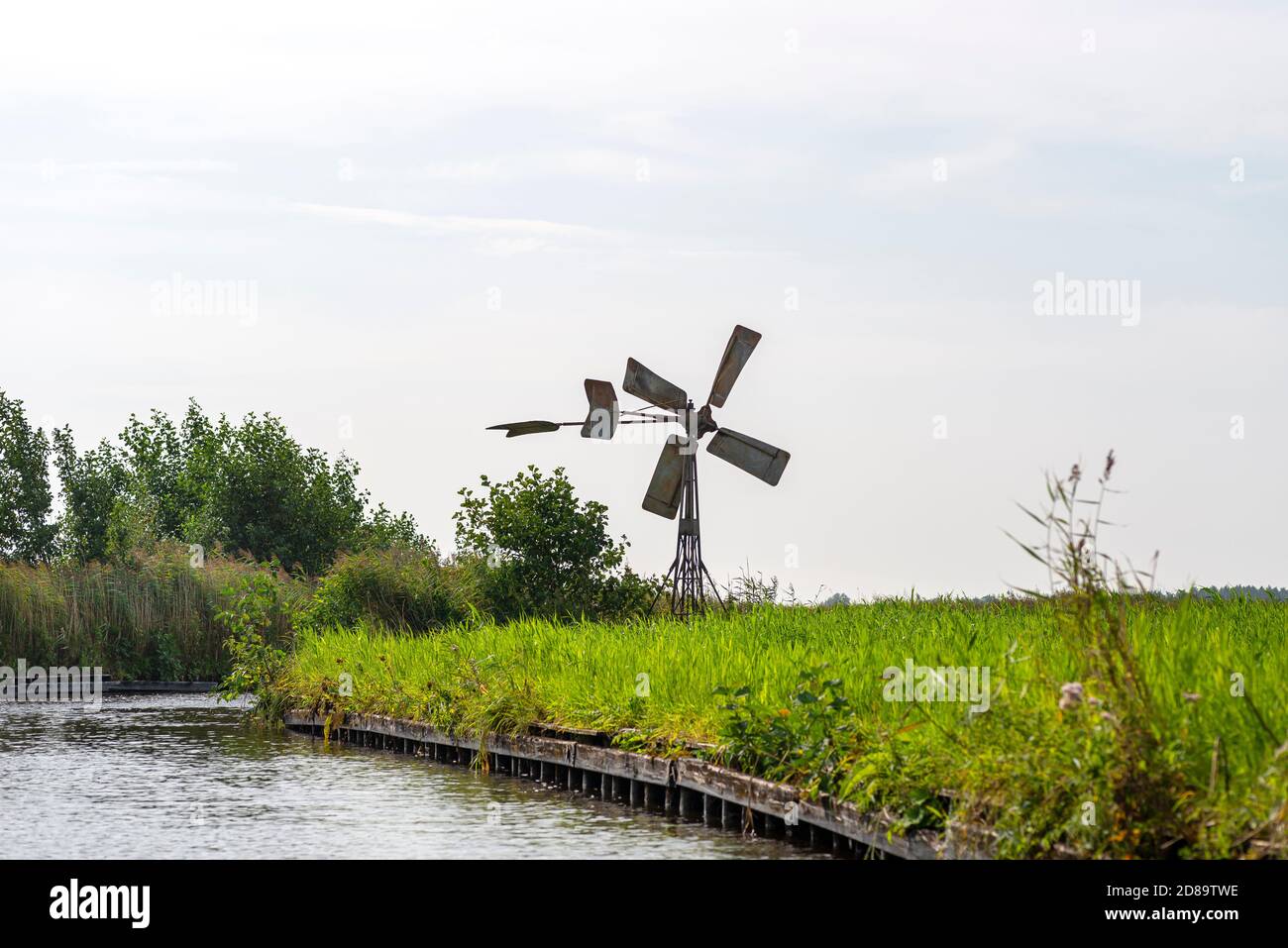 Un moulin à vent en métal se tenant sur la rive d'un canal qui coule dans une rivière aux pays-Bas. Banque D'Images