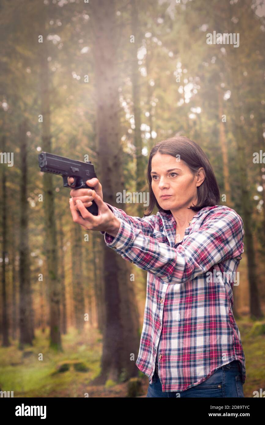 Femme visant un pistolet dans les bois, expression moyenne. Banque D'Images