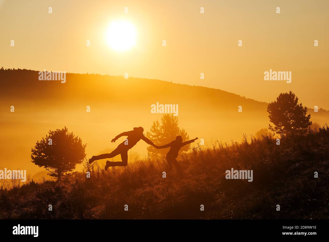 Belle brume le matin. Silhouettes de deux personnes faisant un saut heureux pendant le beau lever de soleil doré. Banque D'Images