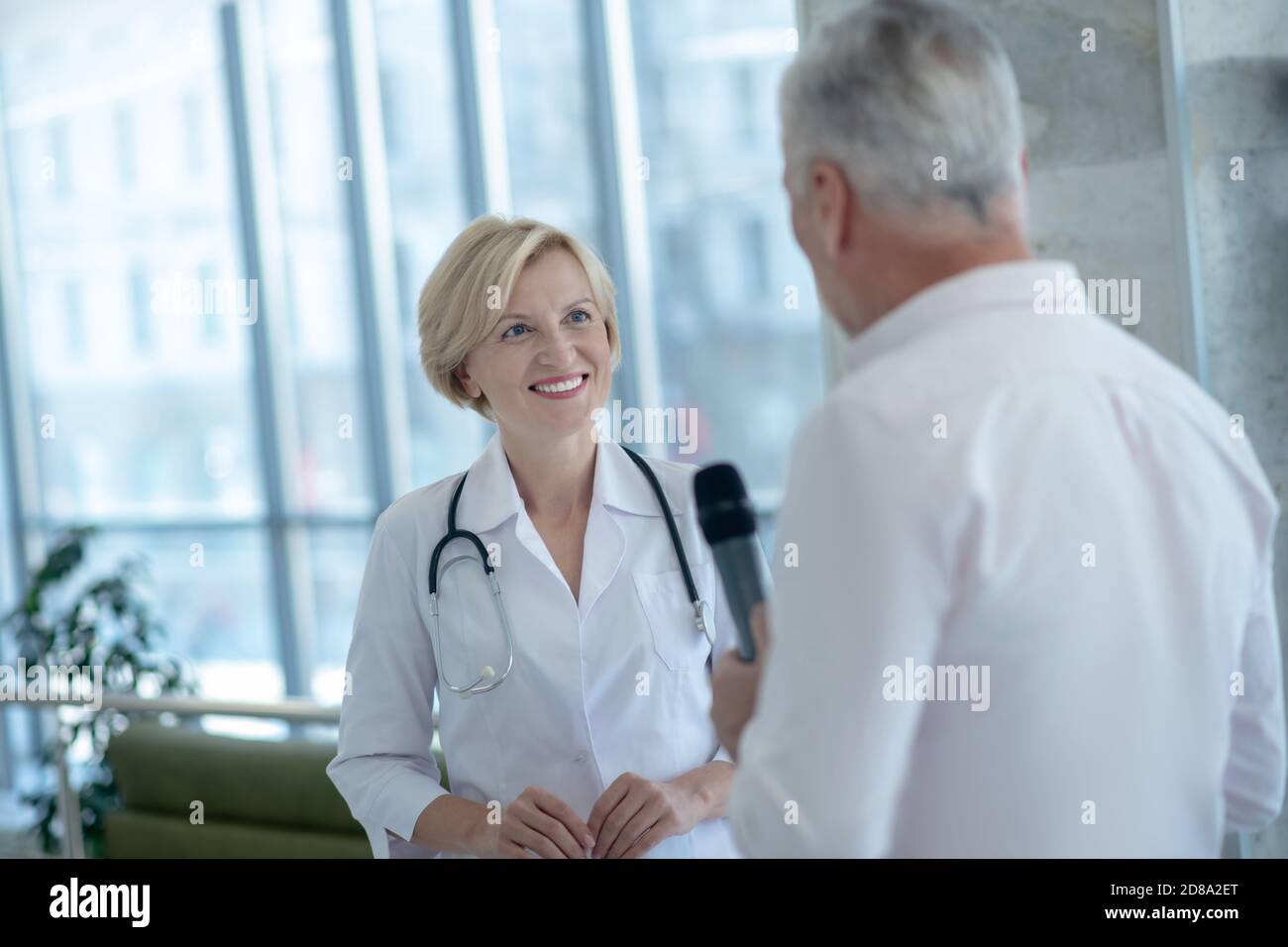 Journaliste mâle aux cheveux gris ayant eu un entretien avec une femme blonde souriante médecin Banque D'Images